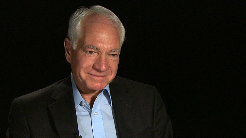 Claude Canizares seated in front of a black background for an on camera interview.