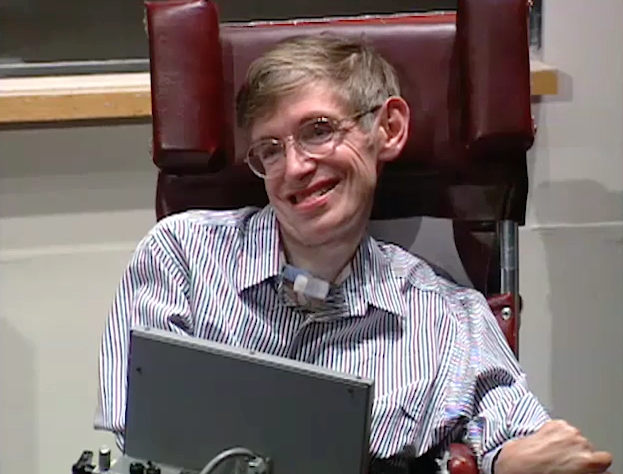 Stephen Hawking lectures in classroom, sitting in wheel chair, chalkboard in the background