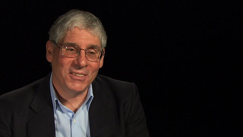 John Essigmann seated in front of a black background for an on camera interview.