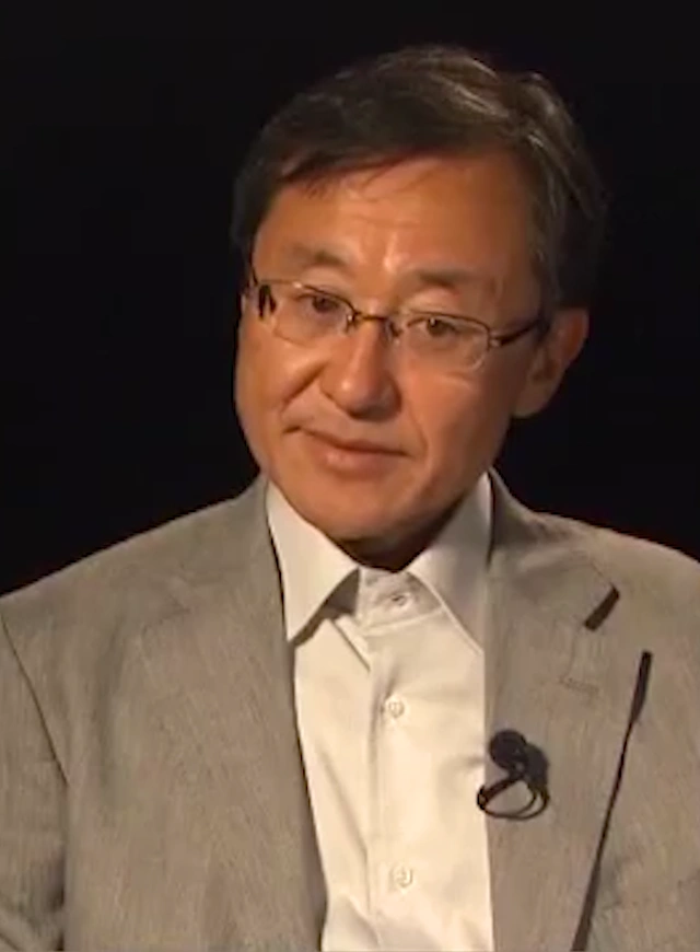 Shigeru Miyagawa seated in front of a black background for an on camera interview.