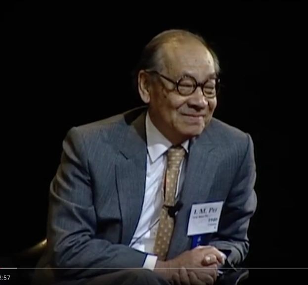I. M. Pei stands in front of a black background with hands clasped, smiling, and looking to the side.