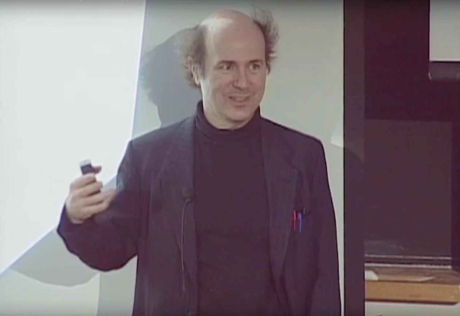 Frank Wilczek speaking in classroom, projector screen and chalkboard in background.