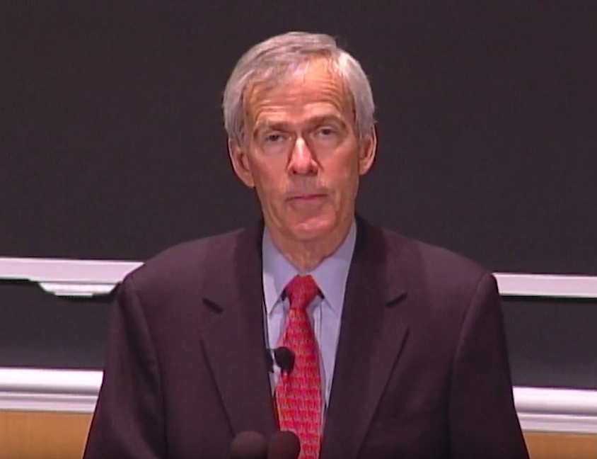 Jeff Bingaman speaking in front of chalkboard