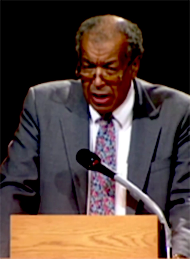 A. Leon Higginbotham speaking at a podium on stage, in front of a dark background
