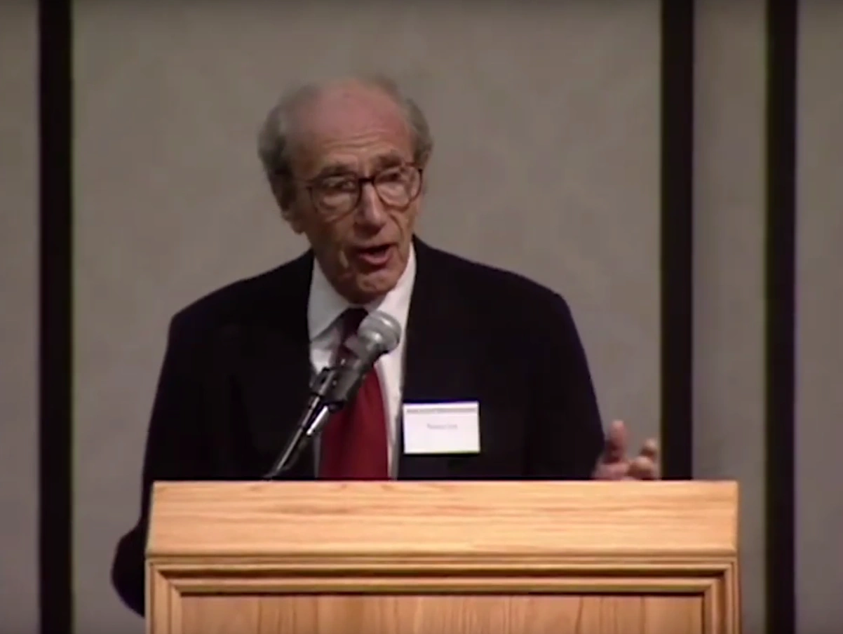Frank A. Wilczek speaking at a podium, cream colored wall in background