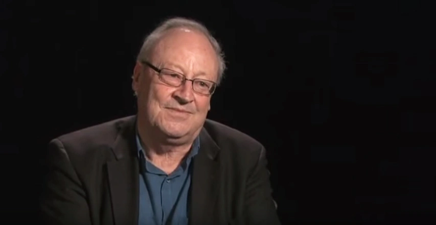 William J. Mitchell seated in front of a black background for an on camera interview.