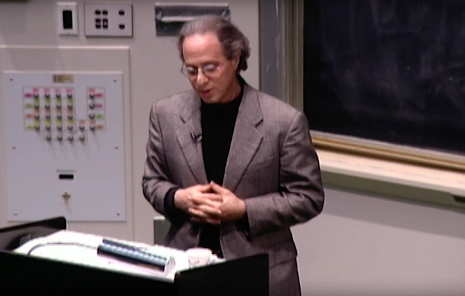 Ray Kurzweil standing at podium in classroom, with a chalkboard in the background.