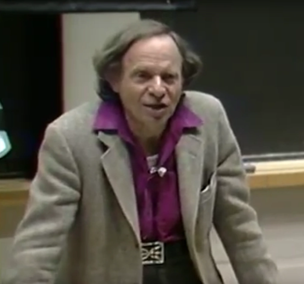 Phillip Morrison delivers a speech at a podium in classroom, chalkboard in the background.