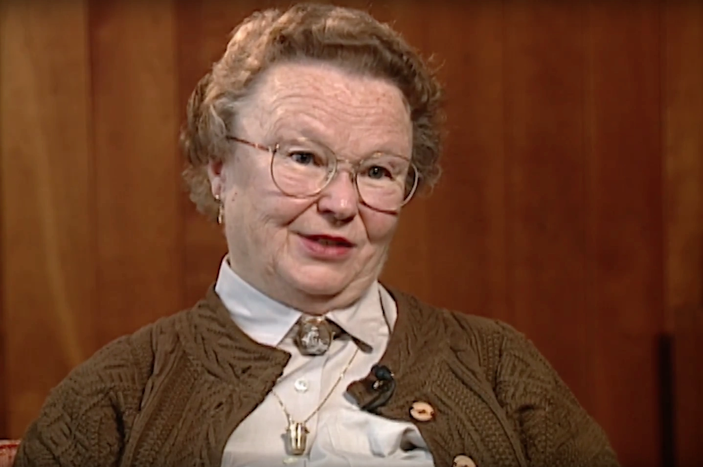 Mrs. Priscilla King Gray seated in front of wood paneled wall