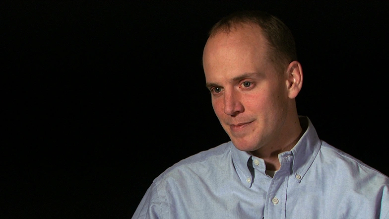 John A. Ochsendorf seated in front of a black background for an on camera interview, looking to the side.