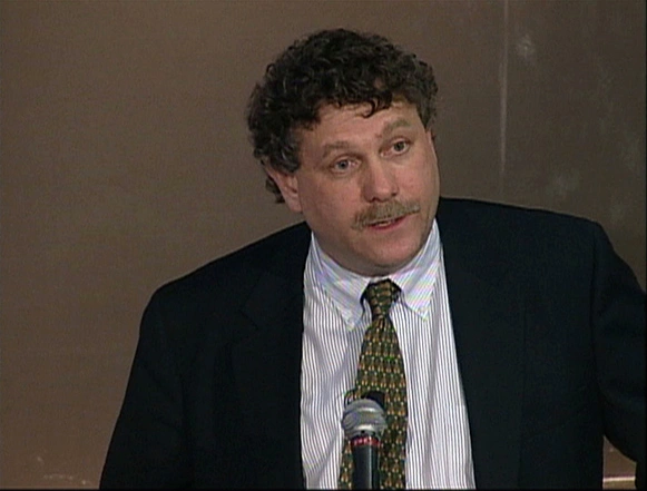 Eric Lander speaking at podium, white wall in background