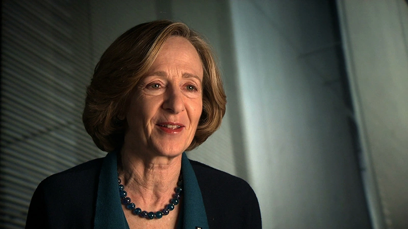 Susan Hockfield seated for an on camera interview, shadowy white walls in the background.