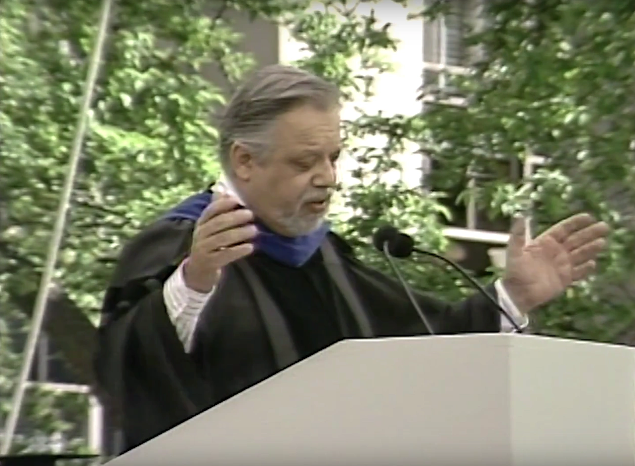 A. Bartlett Giamatti dressed in commencement attire, speaking at a podium on an outdoor stage