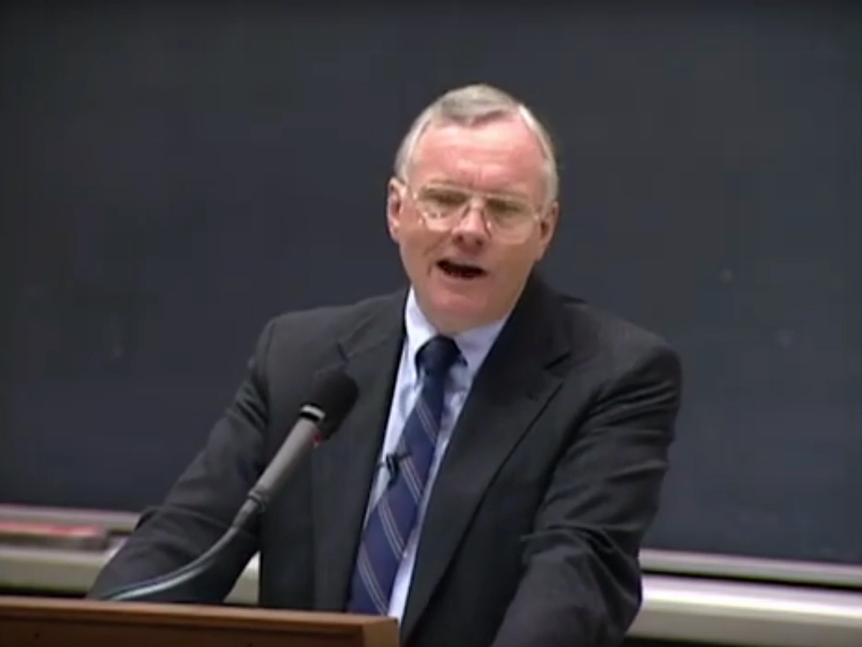 Neil Armstrong speaks at a podium in front of a chalkboard 
