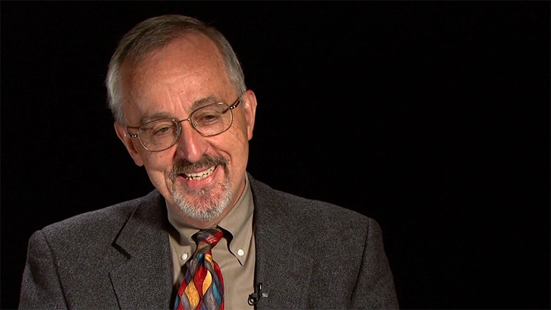 Richard Larson seated in front of a black background for an on camera interview, smiling.