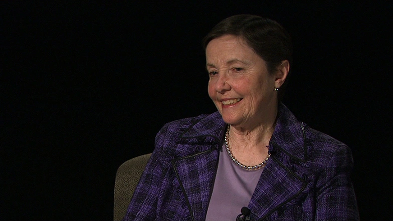 Rebecca M. Vest seated in front of a black background for an on camera interview, smiling
