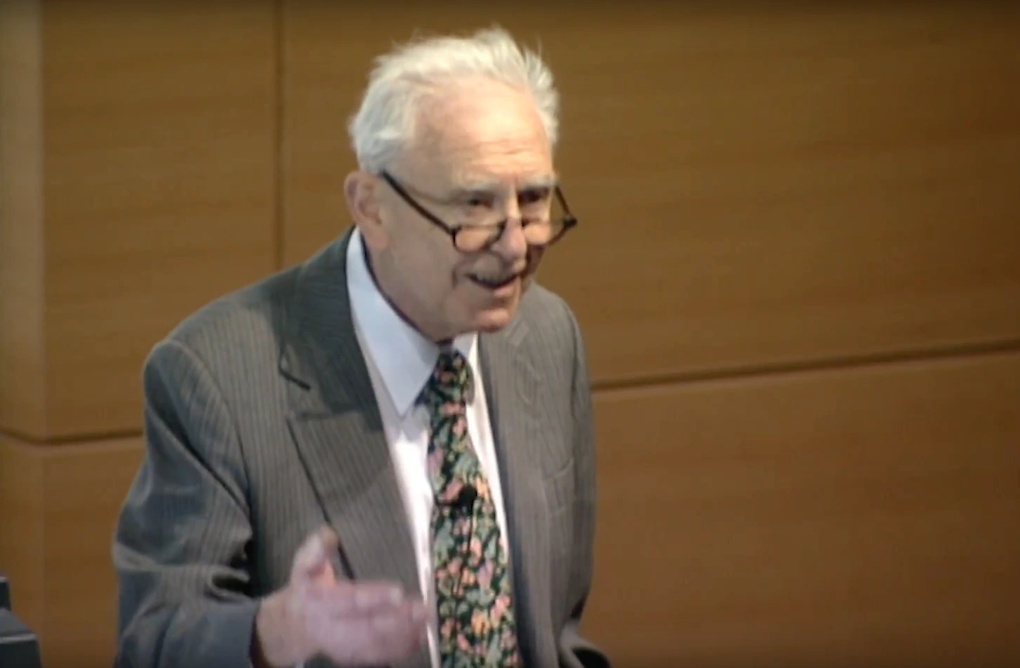 Franco Modigliani speaking on stage, wood paneled walls in the background