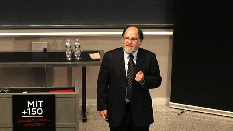 Ronald Rivest delivering speech next to podium, dark blue walls with white wooden accents in background