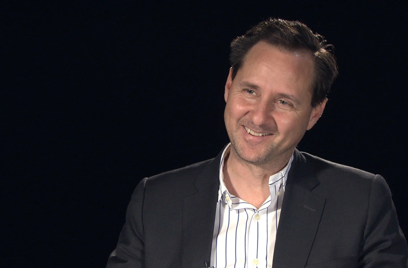Hugh Herr seated in front of a black background for an on camera interview, smiling