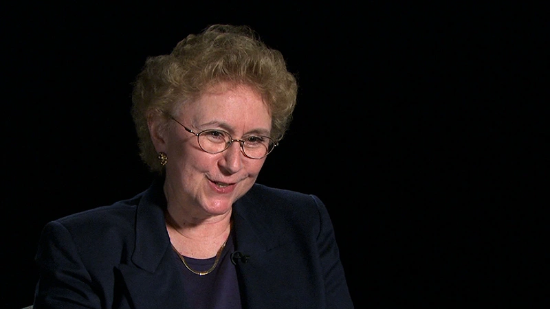 Candace Royer smiling, seated in front of a black background for an on camera interview.