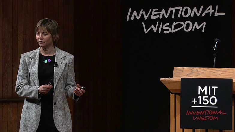 Maria Zuber speaking onstage, a dark backdrop with white MIT150 event branding in the background.