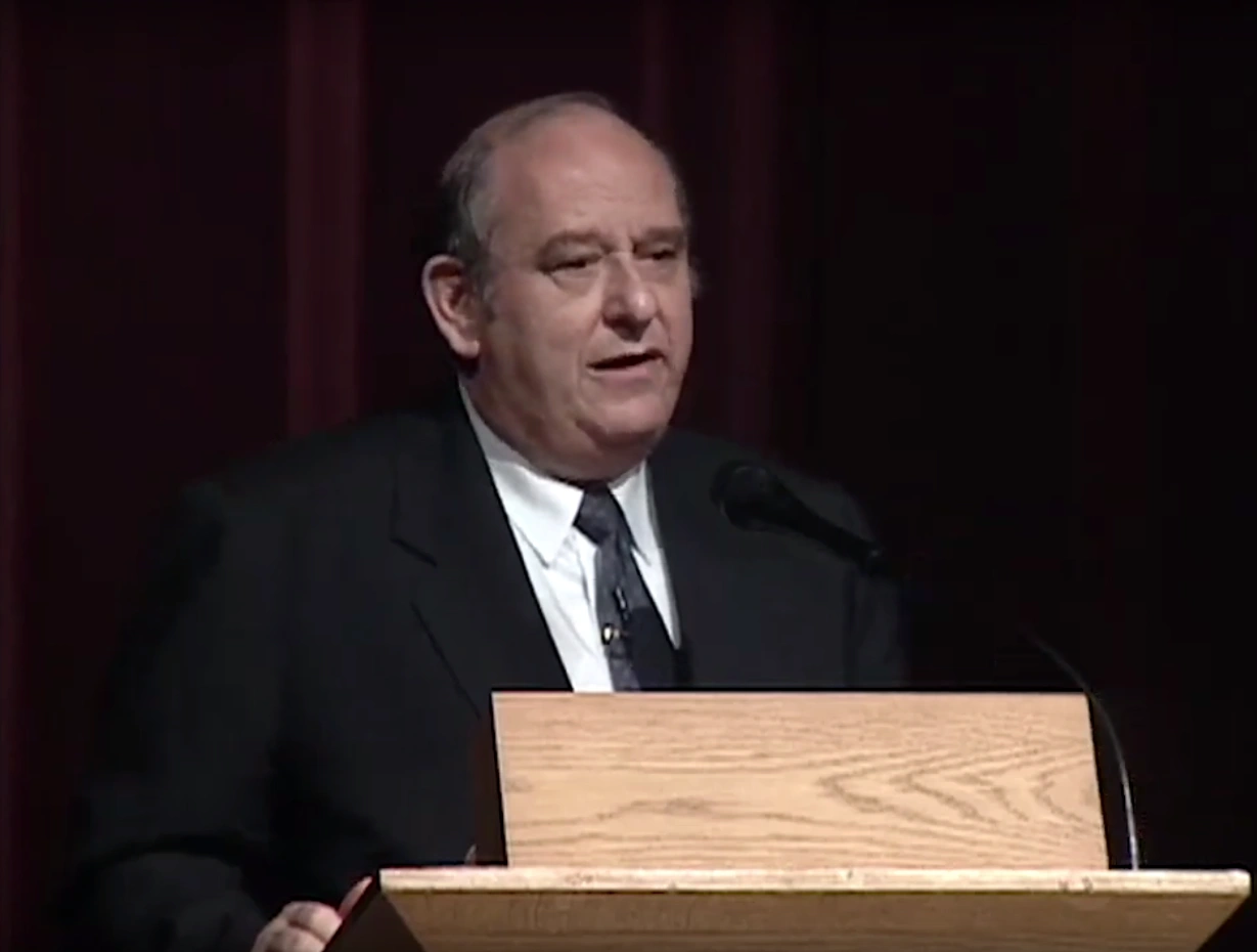 David H. Marks speaking at a podium on stage, in front of a dark background