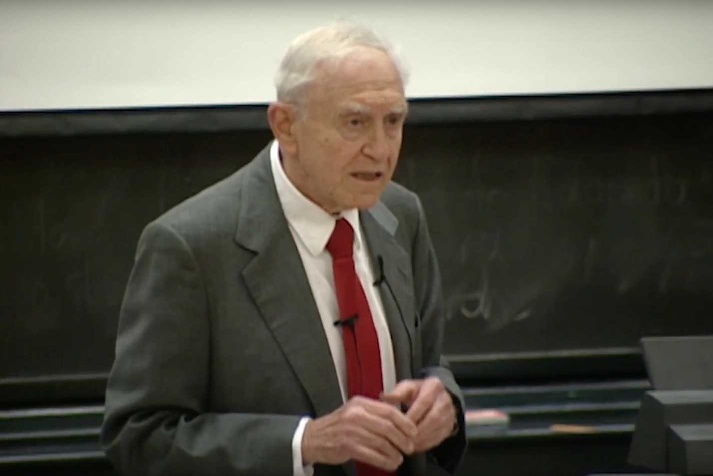Franco Modiglianilecturing in a classroom, standing in front of a chalkboard .