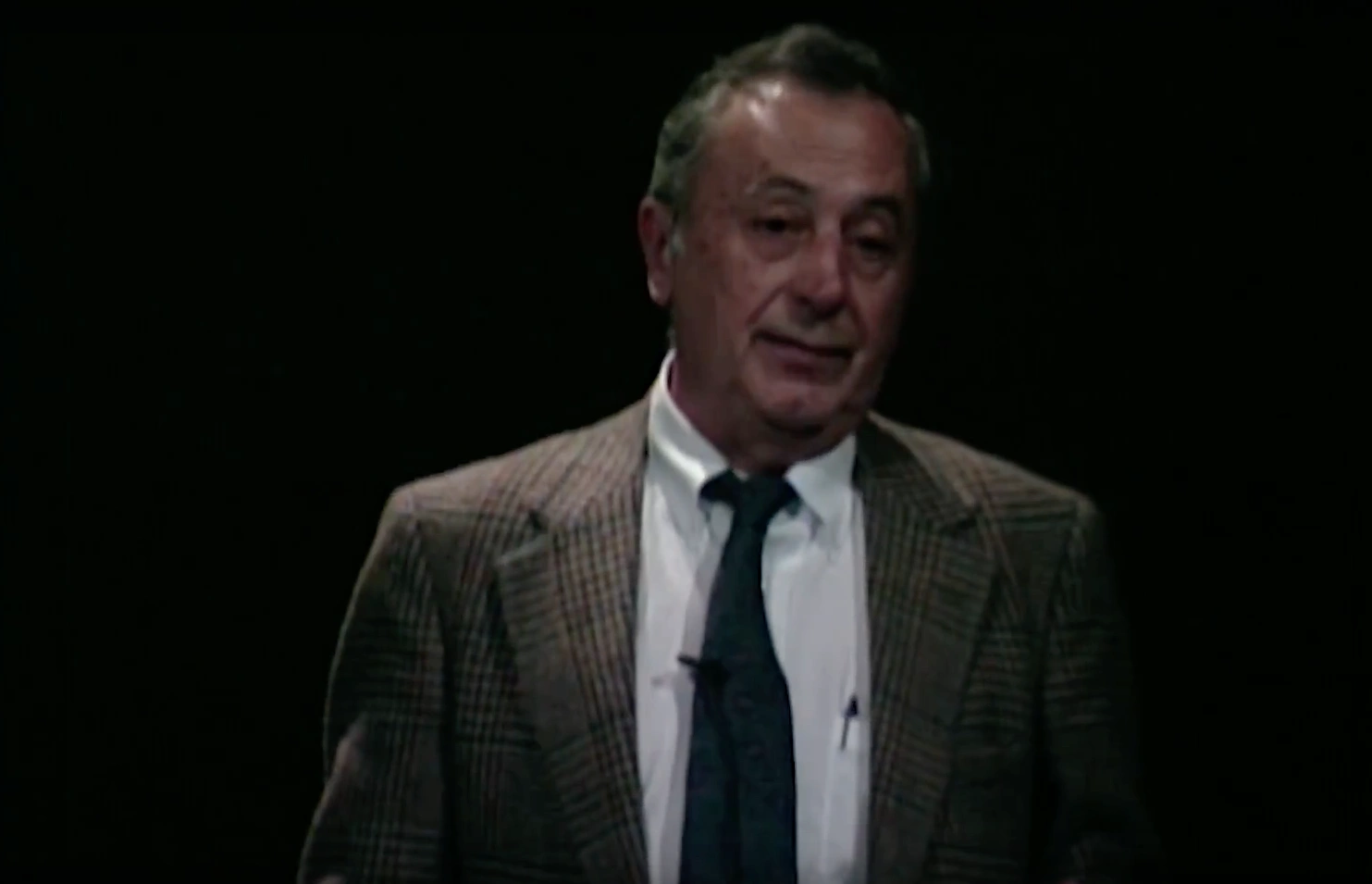 William E. Turchinetz speaking on stage, in front of a dark background