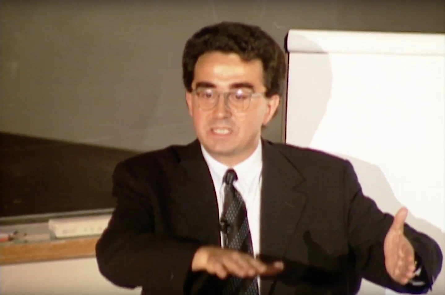 Santiago Calatrava speaking next to a flipchat in a room with white walls.