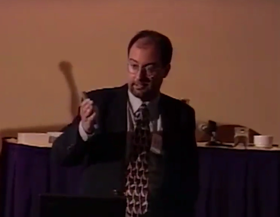 Joseph Mayer Jacobson standing and speaking in a classroom with white walls.