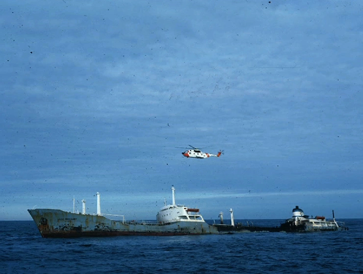 a large ship on the ocean in the distance, a small plane hovering in the cloudy sky above.