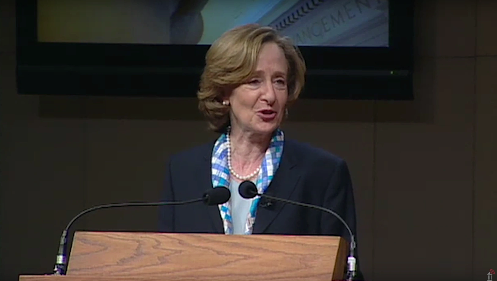 Susan Hockfield speaking at a podium on stage, in front of a dark background