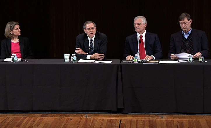 Four panelists for an economic policy panel sit at a long black table on stage.