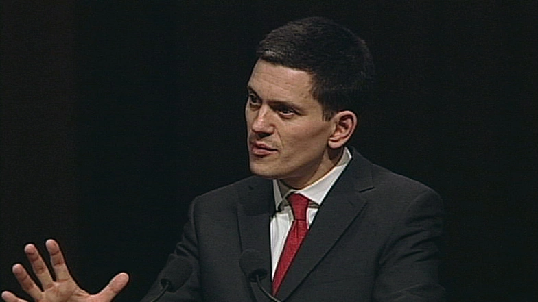 David Miliband speaking onstage in front of a dark background