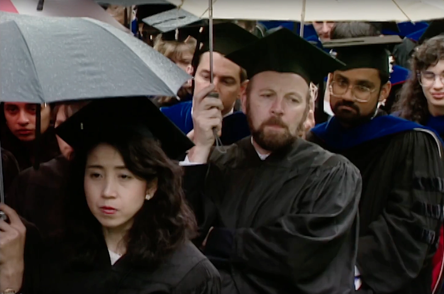 MIT students in caps and gowns holding umbrellas during rainy commencement ceremonies.