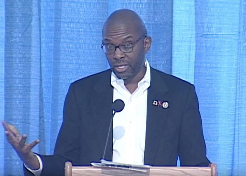 Ted Childs speaking at a podium in front of a blue curtain
