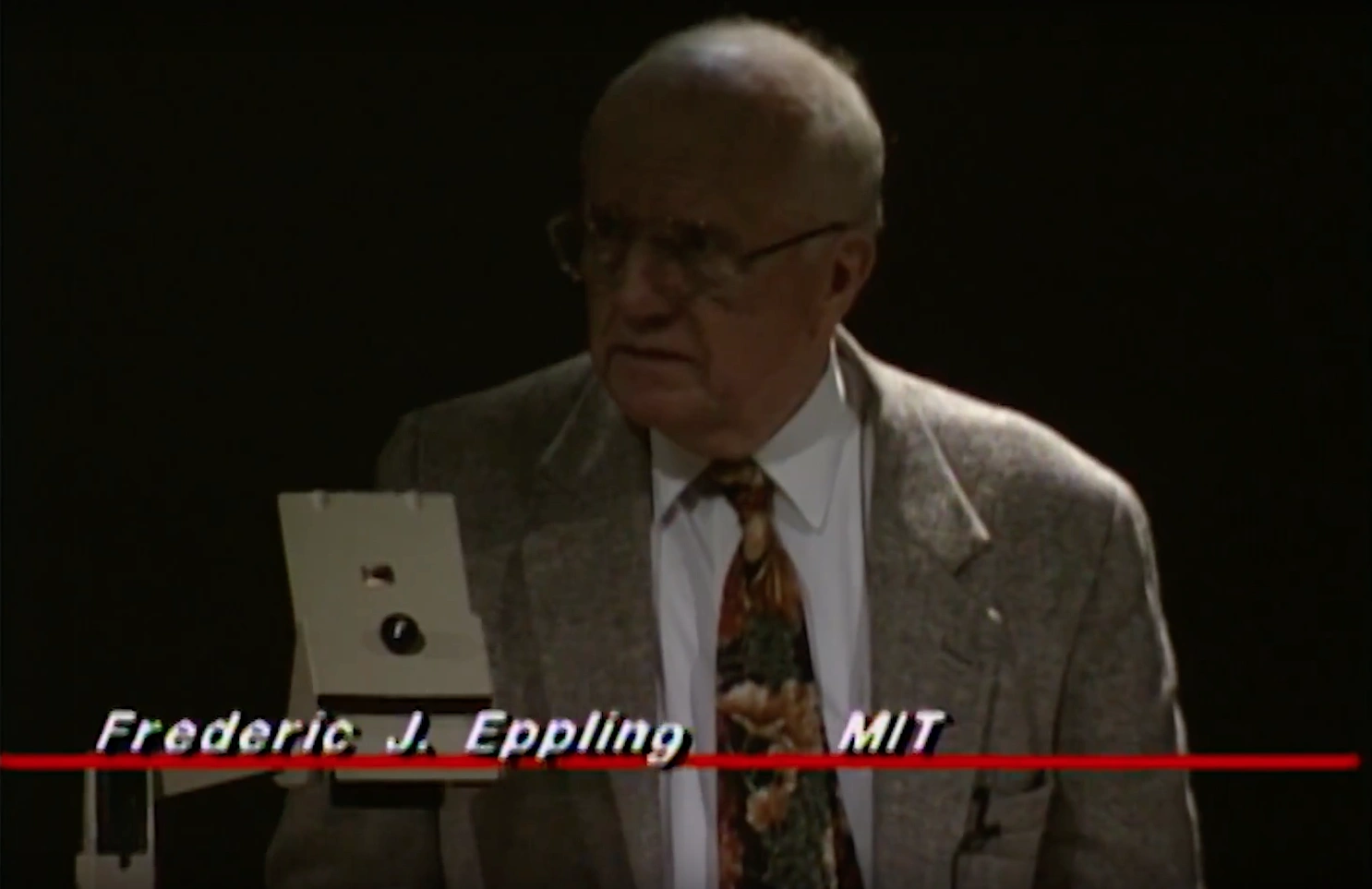 Frederic John Eppling standing on dimly lit stage beside optical microscope, dark curtain in background