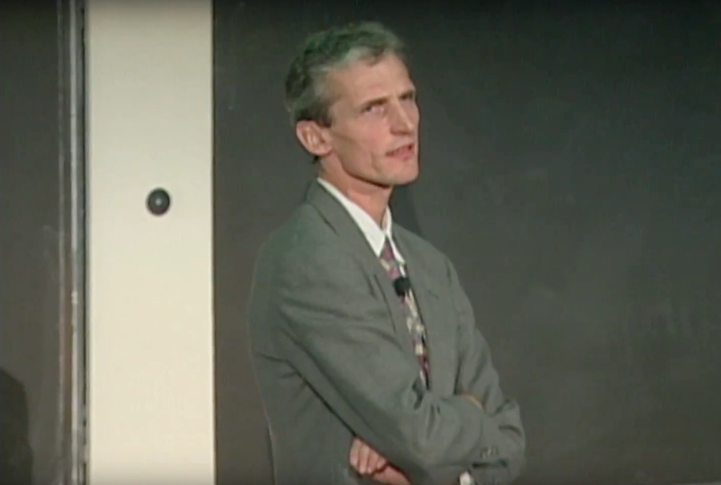 Wolfgang Ketterle stands in front of chalkboard, arms crossed and looking to the sde