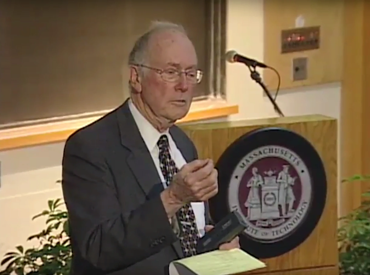 Charles Townes speaks in classroom, standing in front of podium, chalkboard in the background