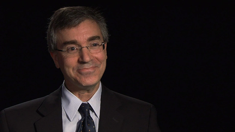 Stuart Schmill seated in front of a black background for an on camera interview, smiling.