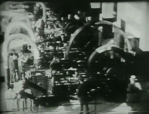 Man standing in front of machine comprised of large wheels, pistons, tubing