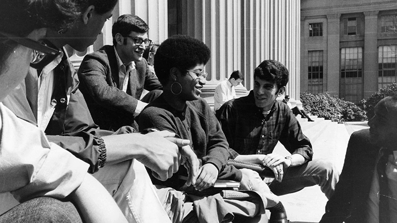 Students sit on the steps of MIT's Building 10. A black and white photograph.