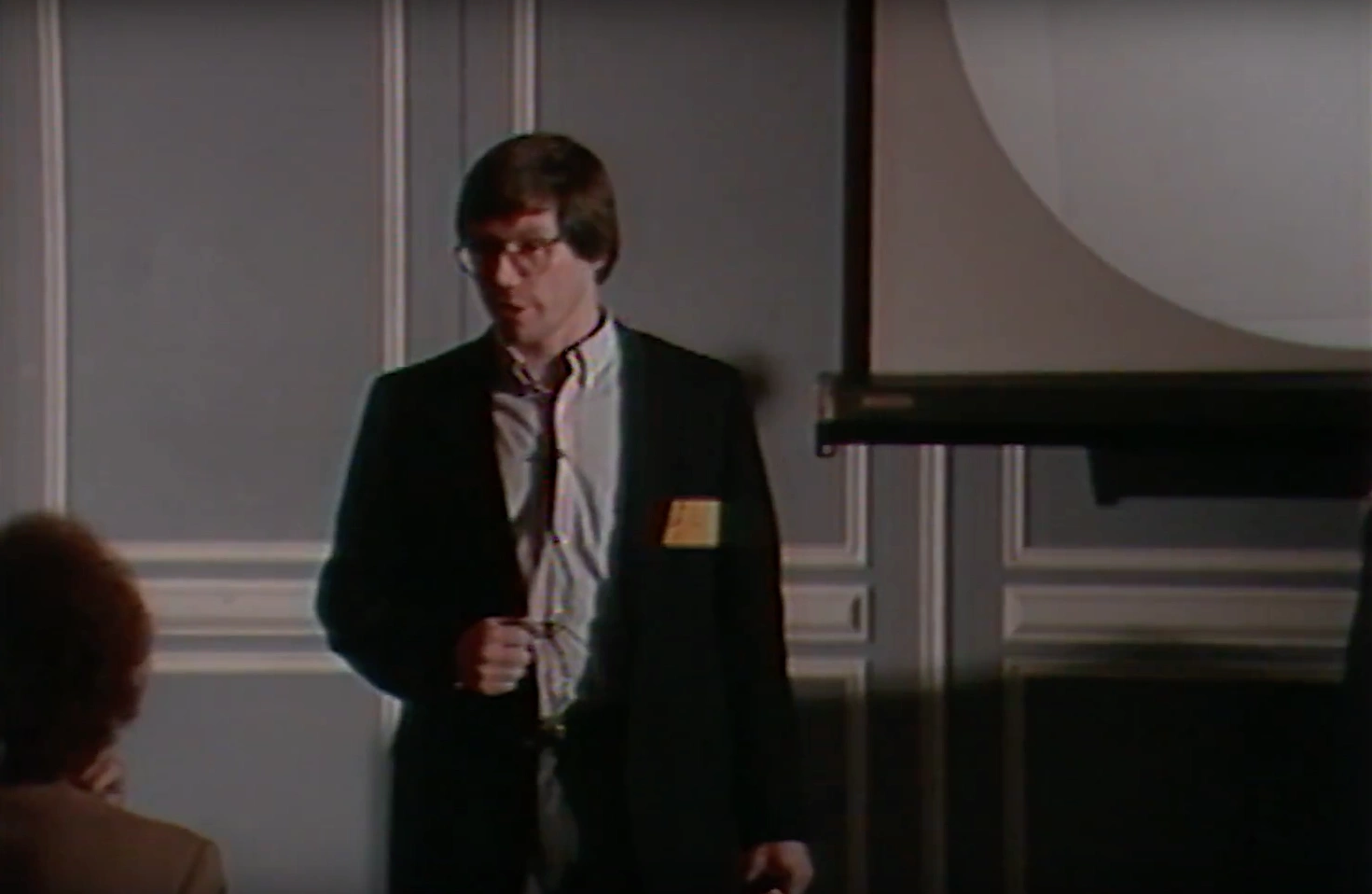 Alan Guth standing in banquet room, speaking to seated attendees in front of projection screen.