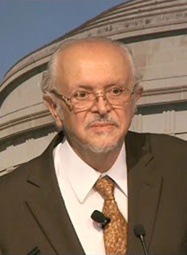 Mario Molina delivers a lecture onstage, a large image of MIT's great dome building in the background