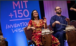 Two students playing drums in front of MIT 150 banner