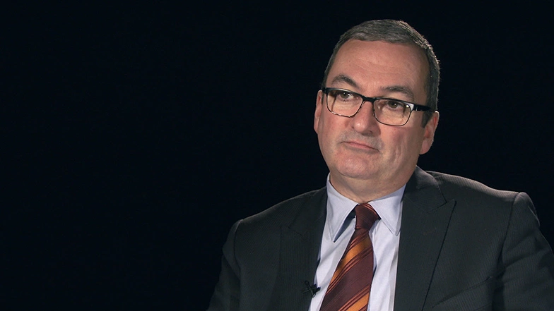 David Maher seated in front of a black background for an on camera interview.
