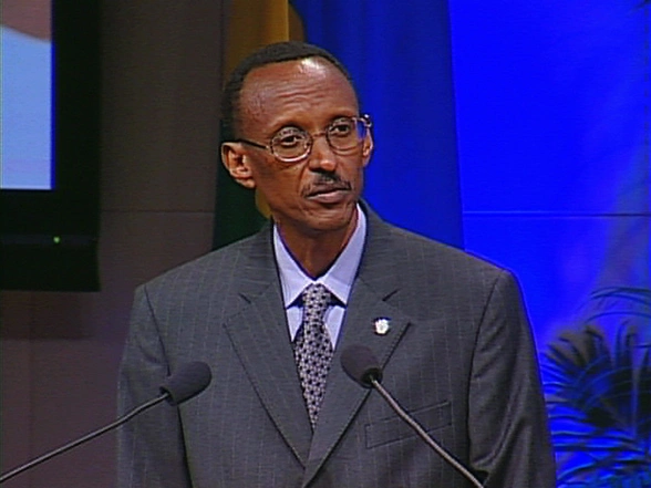Paul Kagame speaks into podium microphones onstage, a bright blue screen in the background