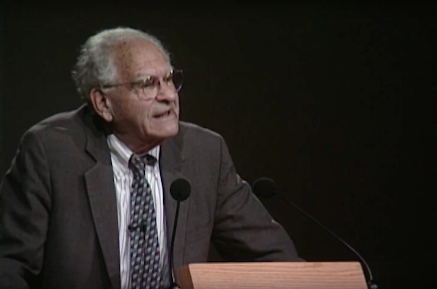 Victor Weisskopf speaking at a podium on stage, in front of a dark background
