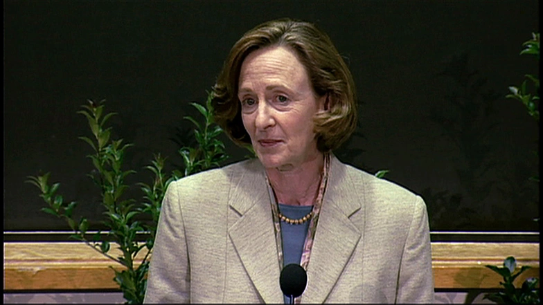 Susan Hockfield speaks at a podium in a classroom, chalkboard in background