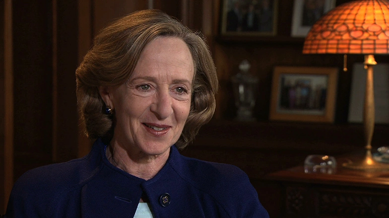 Susan Hockfield seated for an on camera interview in cozy living room with stained glass table lamp.